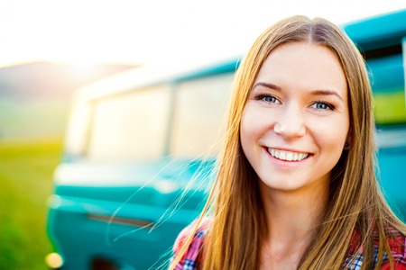 Teenage girl with long hair smiling against green campervan outside in sunny nature