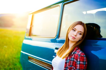 Teenage girl with long hair smiling leaning against green campervan outside in sunny nature
