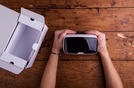 Hands of man holding virtual reality goggles. Flat lay. Studio shot on wooden background.