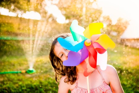 Beautiful girl in swimsuit hiding behind colorful pinwheel, sunny summer garden