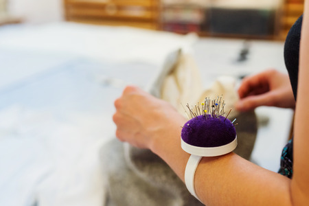 Close up of hands of unrecognizable tailor woman with pin cushion on hand working