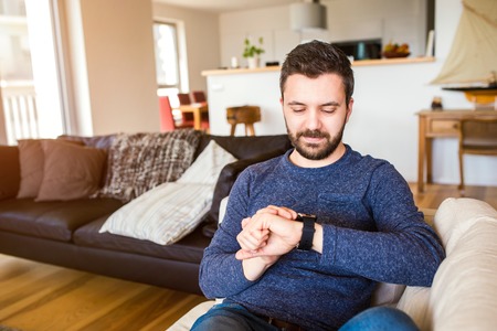 Casual hipster man working from home using smart watch, sitting in living room