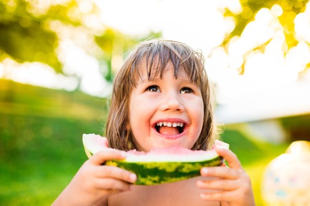 Cute little girl eating watermelon outside in garden, sunny summer back yardの写真素材