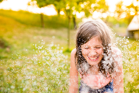 Girl in bikini sitting at the sprinkler, green sunny summer gardenの写真素材
