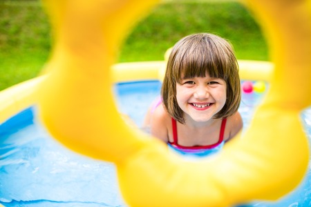 Cute little girl having fun in garden swimming pool. Sunny summer day at the backyard