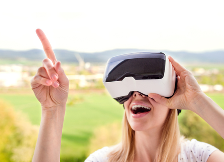 Blond woman wearing virtual reality goggles standing in a kitchen