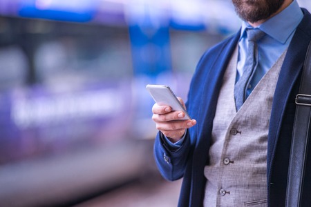Unrecognizable businessman with smartphone, waiting at the train station platformの写真素材