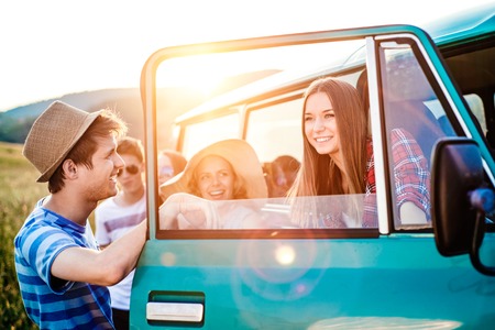 Group of teenage hipsters on a roadtrip having fun, standing at the campervan. Young friends outside on a summer day.の写真素材