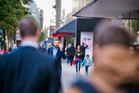 Hipster manager holding a smart phone, making a phone call, walking in the street of Londonの写真素材