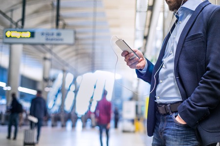 Close up of unrecognizable hipster businessman with smartphone standing on subway station listening musicの写真素材