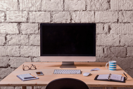 Desk with various gadgets and office supplies. Computer, smart phone and stationery around the workplace. White brick wall.の写真素材