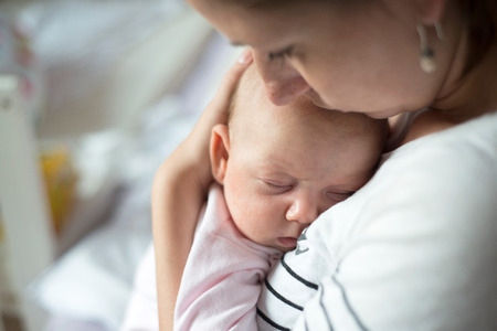 Close up of young mother holding her cute baby daughter, kissing her