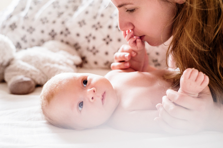 Cute newborn baby boy lying on a bed, held by his motherの写真素材