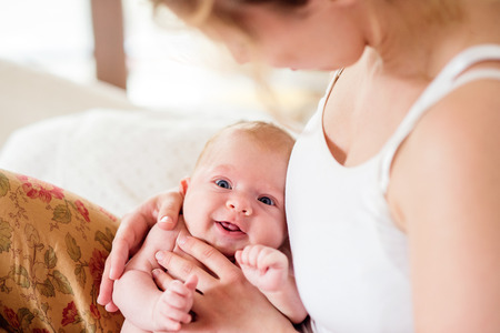 Young mother holding her cute newborn baby son, home bedroomの写真素材