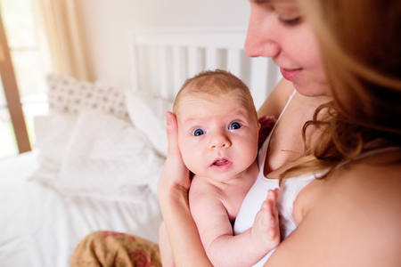 Young mother holding her cute newborn baby son, home bedroomの写真素材