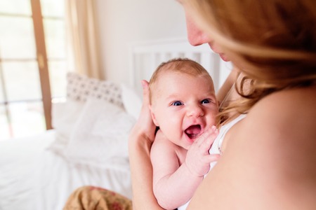 Young mother holding her cute newborn baby son, home bedroomの写真素材
