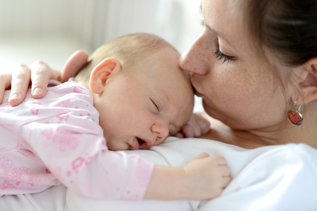 Close up of young mother holding her cute baby daughter lying on her, sleeping, kissing herの写真素材