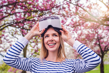 Blond woman wearing virtual reality goggles outside in spring natureの写真素材
