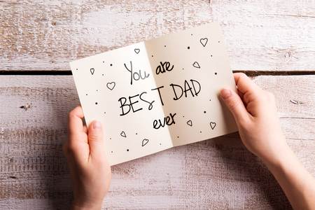 Hands of unrecognizable man holding Fathers Day greeting card. Studio shot on white wooden background.の写真素材