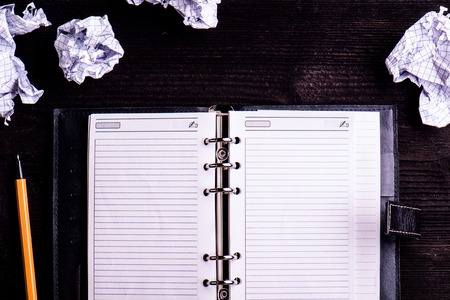 Personal organizer, pen and crumpled paper balls on an old table, copy space. Studio shot on dark wooden background.の写真素材