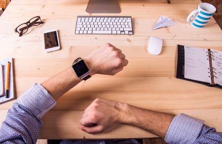 Businessman at the desk, wearing smart watch, working.  Computer, smart phone and various office supplies around the workplace.の写真素材