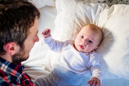Cute newborn baby boy lying on a bed, with his fatherの写真素材