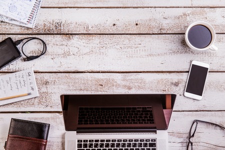 Desk with gadgets and office supplies. Laptop, smart phone and notepads around the workplace. Flat lay. Studio shot on white wooden background. Copy spaceの写真素材