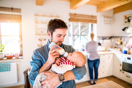 Young father feeding his cute newborn baby son, holding him in his armsの写真素材