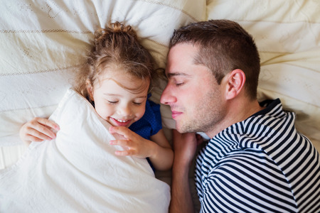 Father and daughter lying in parents bed, sleeping and smilingの写真素材