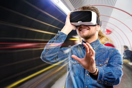 Hipster man in denim shirt wearing virtual reality goggles. Subway station.