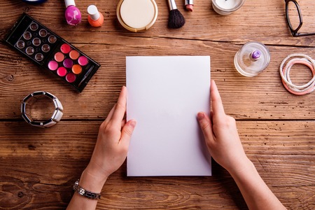 Hands of unrecognizable woman holding empty greeting card. Various make up products. Studio shot on wooden background. Copy space.の写真素材
