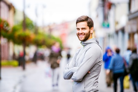 Young hipster man in gray sweatshirt running in town, resting, main streetの写真素材