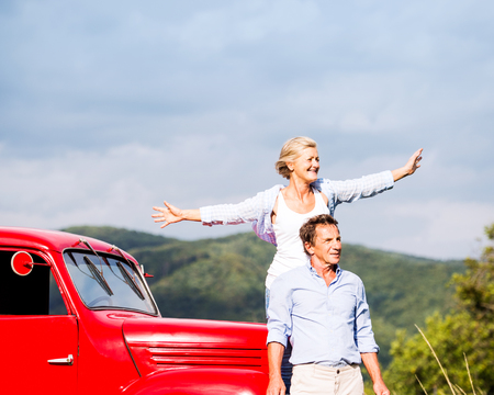 Senior couple standing at the red vintage car, green sunny natureの写真素材