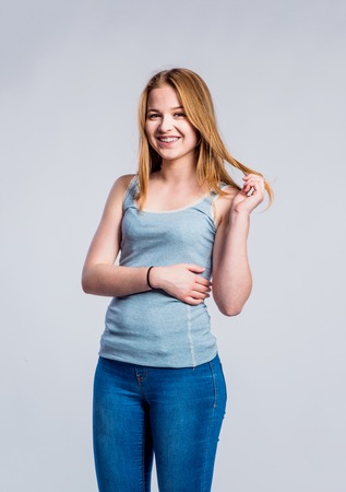 Teenage girl in jeans and blue tank top, young woman, studio shot on gray backgroundの写真素材
