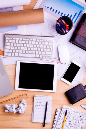 Desk with gadgets, office supplies and chart graph. Computer keyboard, tablet, smart phone and stationery around the workplace. Flat lay. Studio shot on wooden background.の写真素材