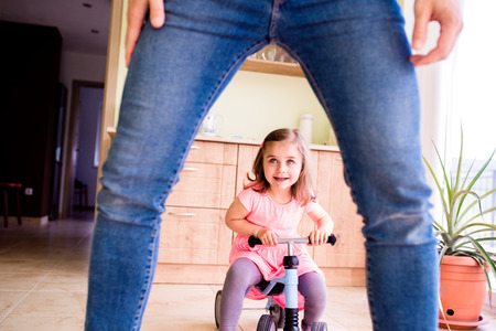 Unrecognizable father and daughter playing together, riding a bike indoors, sunny dayの写真素材