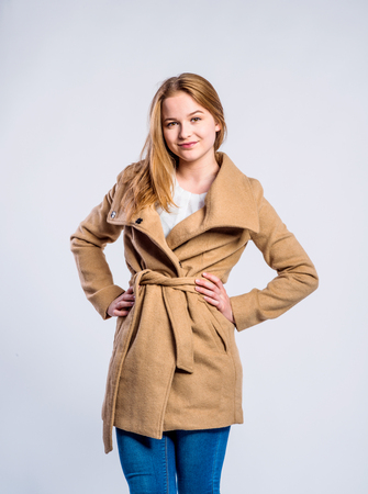 Teenage girl in jeans and brown coat, young woman, studio shot on gray backgroundの写真素材