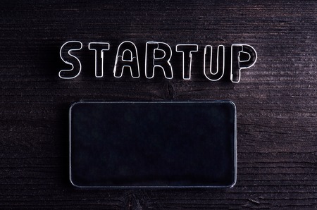 Smart phone and start up sign made of cookie cutters. Studio shot on dark wooden background. Flat lay. Copy space.の写真素材