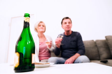 Senior woman and man sitting in living room on sofa, drinking champagneの写真素材