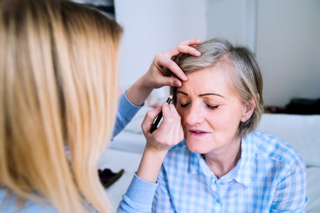 Unrecognizable girl applying make up to a senior woman in checked blue shirtの写真素材