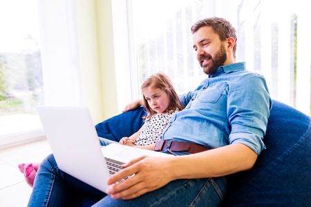 Father and daughter together, playing on laptop, sitting on bean bag, high angle viewの写真素材