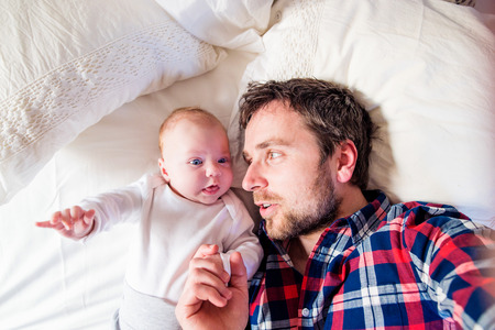 Cute newborn baby boy lying on a bed, next to his fatherの写真素材