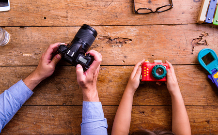 Hands of unrecognizable father and son holding cameras, old office desk. Studio shot on wooden background. Flat lay.の写真素材
