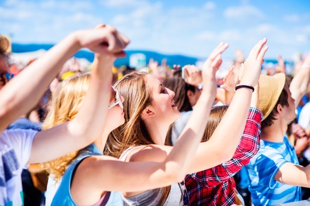 Teenagers at summer music festival under the stage in a crowd enjoying themselves, arm raisedの写真素材