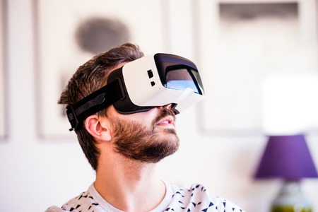 Young hipster man wearing virtual reality goggles, sitting in living roomの写真素材