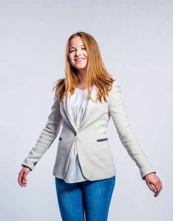 Teenage girl in jeans and beige jacket, young woman, studio shot on gray background