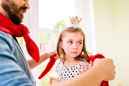 Hipster father with his cute little princess daughter in red super hero cape, dressing herの写真素材