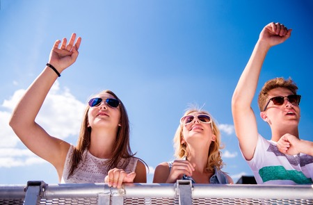 Teenagers at summer music festival, standing under the stage at the crowd control barrier, enjoying themselves, arms raisedの写真素材