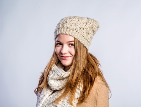 Teenage girl in brown coat and woolen scarf and hat, young woman, studio shot on gray backgroundの写真素材