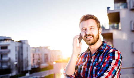 Hipster businessman in checked shirt with smart phone making a phone call, standing on balconyの写真素材